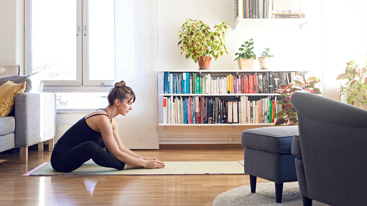 A woman is doing yoga in the living room; image used for "live within your means" article.