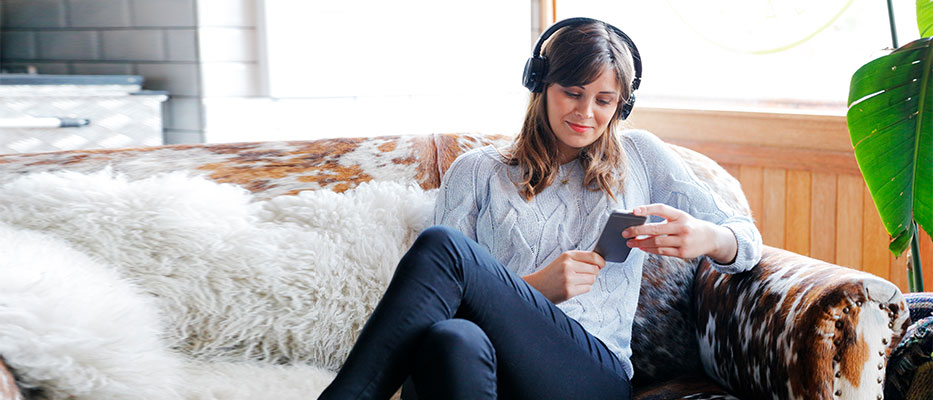 Person wearing headphones on the sofa using their mobile; image used for "healthy habits" article.