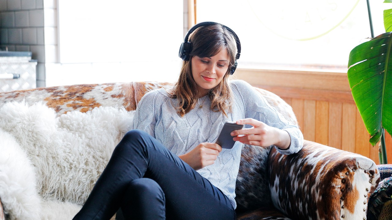 Person wearing headphones on the sofa using their mobile; image used for "healthy habits" article.