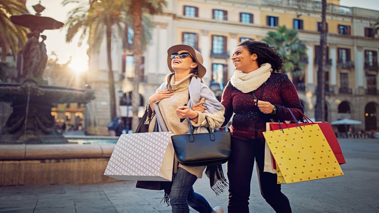 Two young women walking together happily holding many shopping bags; image used for HSBC premier rewards page.