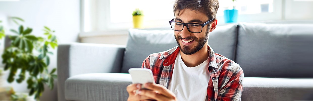 a young man holding a mobile phone smilling; image used for HSBC LK online bill payment page