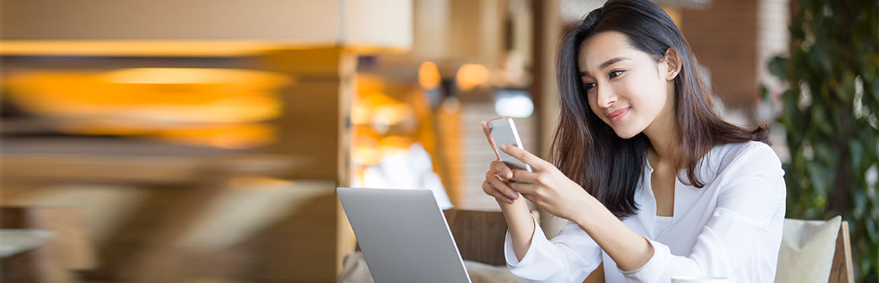 A women is using smartphone and laptop; image used for HSBC ways to bank web chat page.