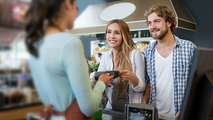 A young couple is paying via a POS device holding by a staff in a coffee shop; image used for HSBC Sri Lanka contactless page.