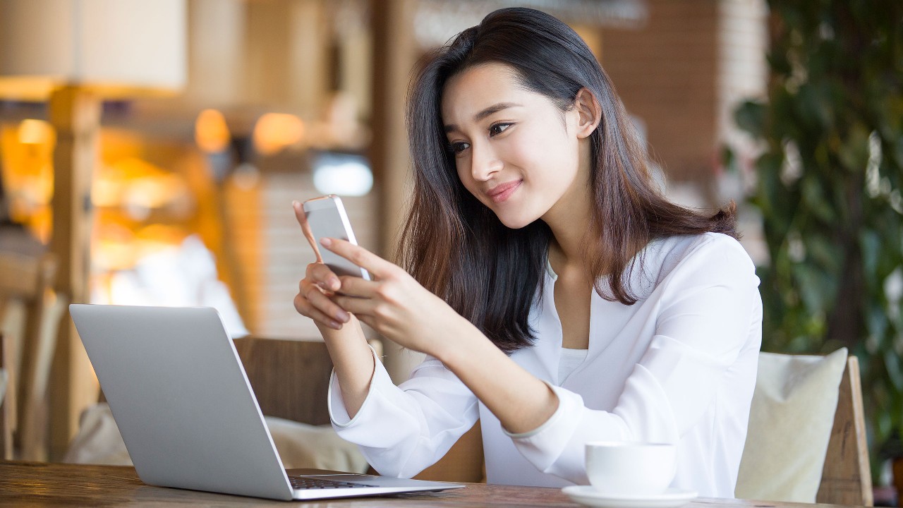 A women is using smartphone and laptop; image used for HSBC ways to bank web chat page.